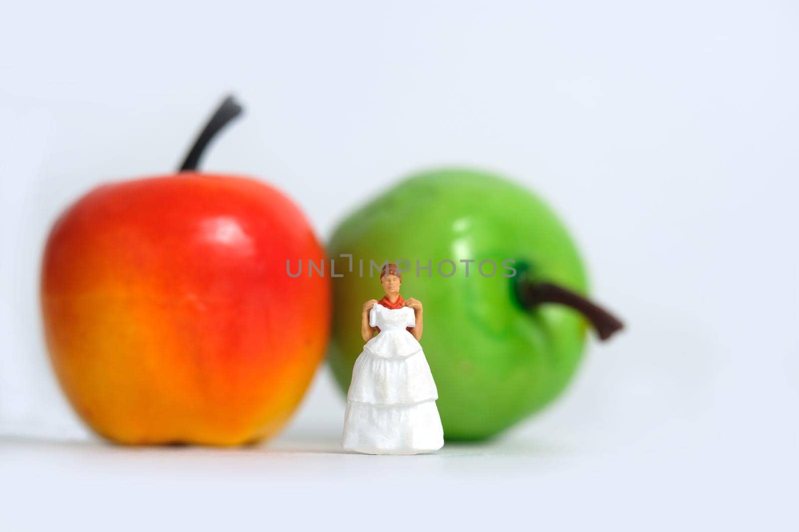 Diet plan before wedding or marriage day concept. Woman standing in front of apple with trying wedding dress. Miniature people, toys photography.