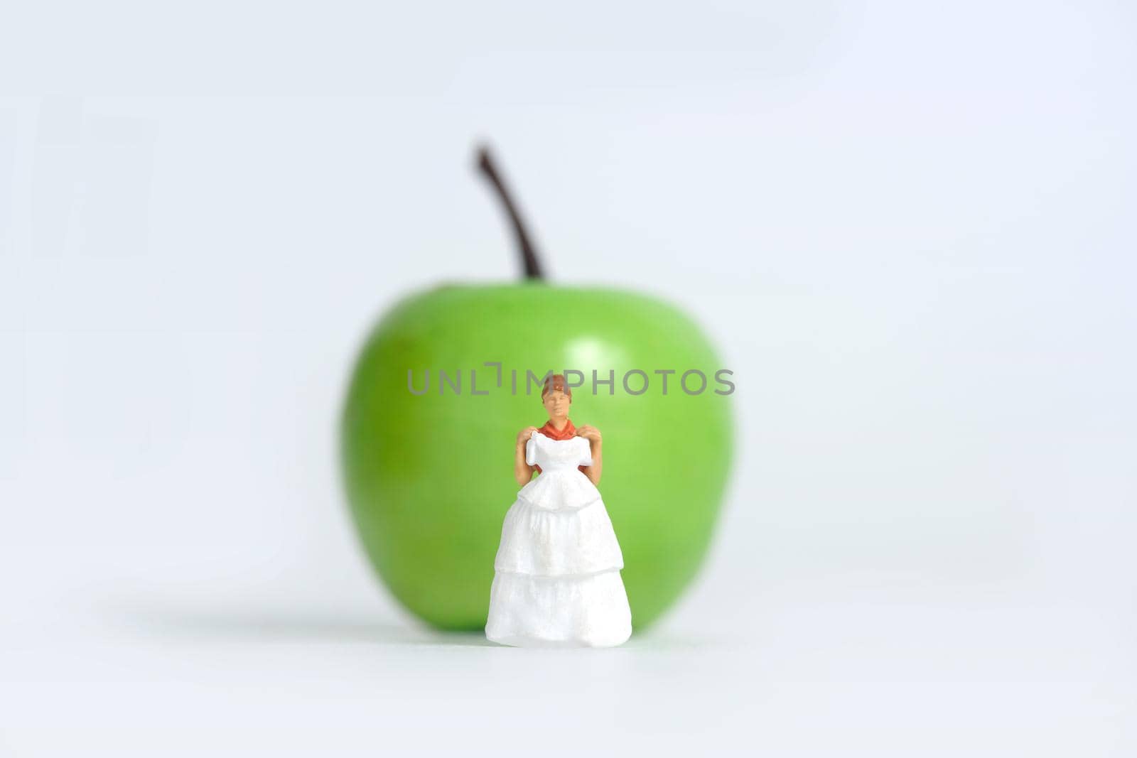Diet plan before wedding or marriage day concept. Woman standing in front of apple with trying wedding dress. Miniature people, toys photography. by Macrostud