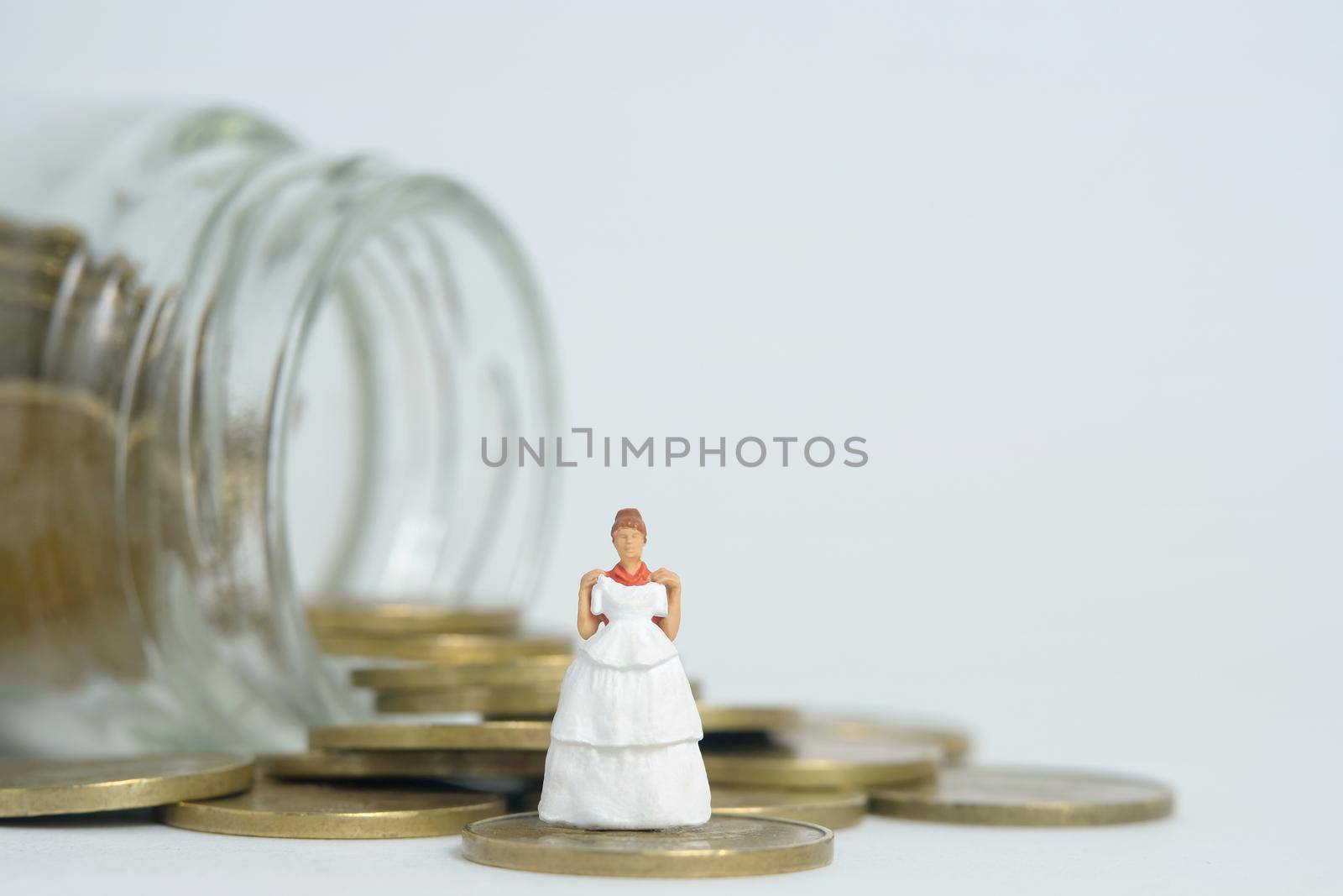 Wedding dress budget for bride, miniature people illustration concept. Woman standing above coin money jar. Image photo by Macrostud