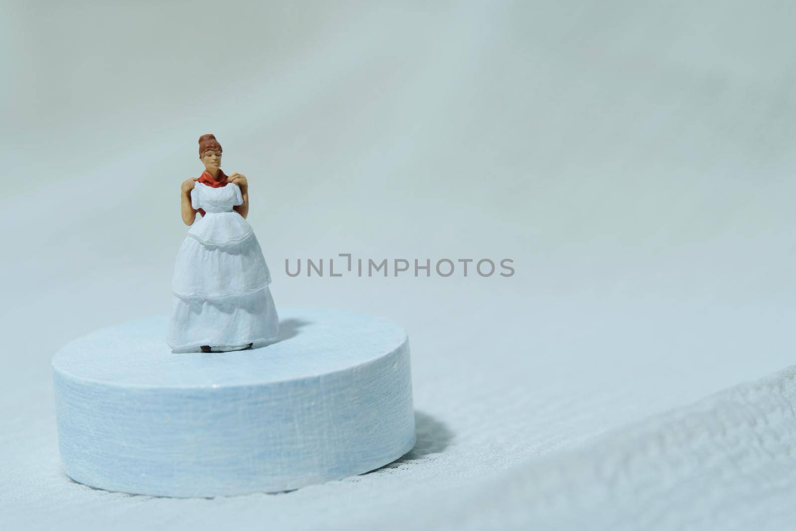 Women miniature people stand above white podium trying wedding dress. Image photo by Macrostud