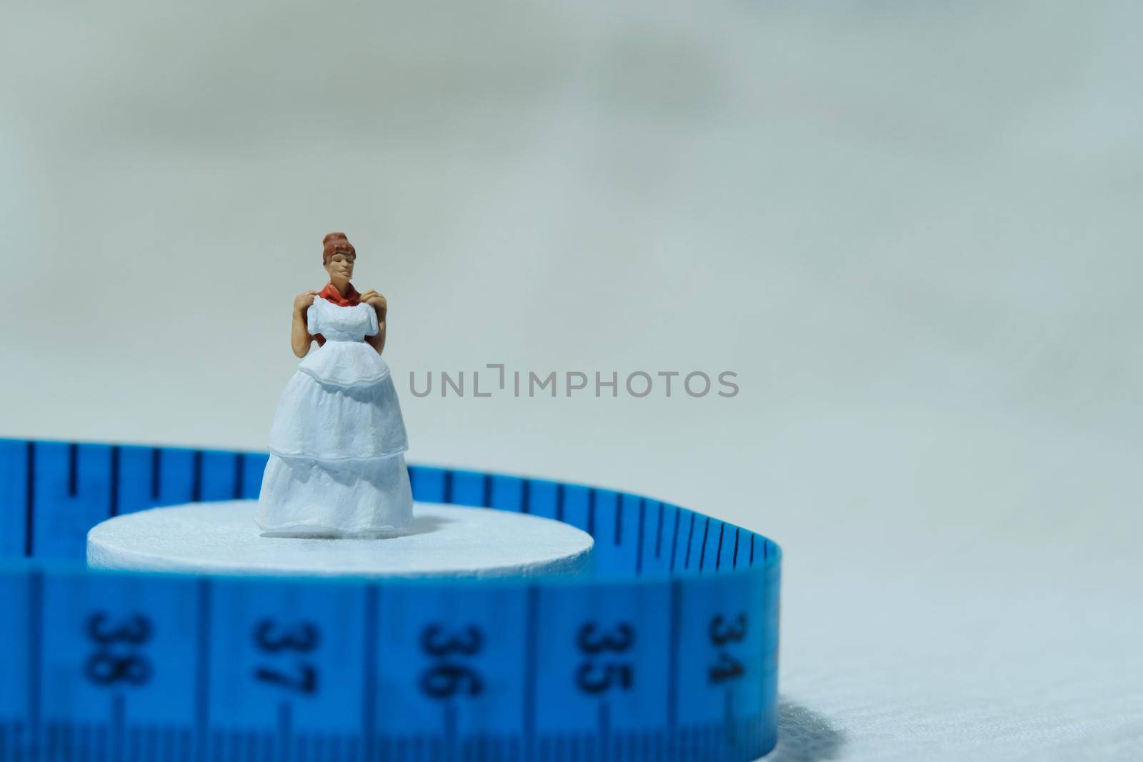 Women miniature people standing above measuring tape to fix her wedding dress. Image photo by Macrostud