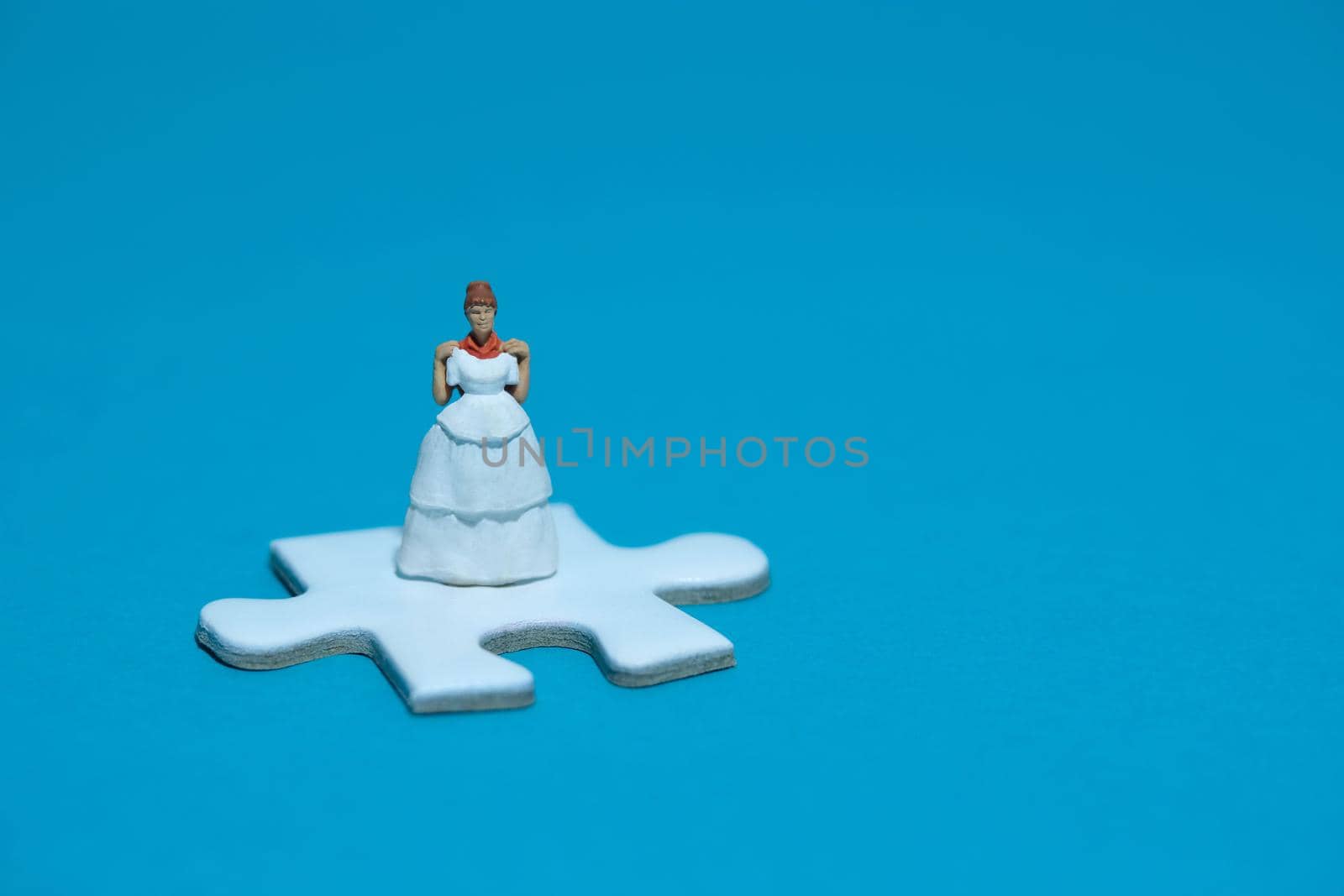 Wedding dress alternative. Miniature people women standing above puzzle jigsaw on blue background by Macrostud