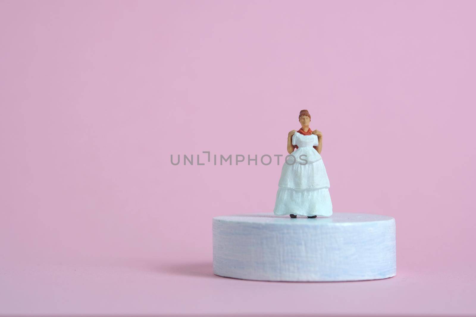 Women miniature people trying to choose wedding dress standing above platform pedestal on blue pink background by Macrostud