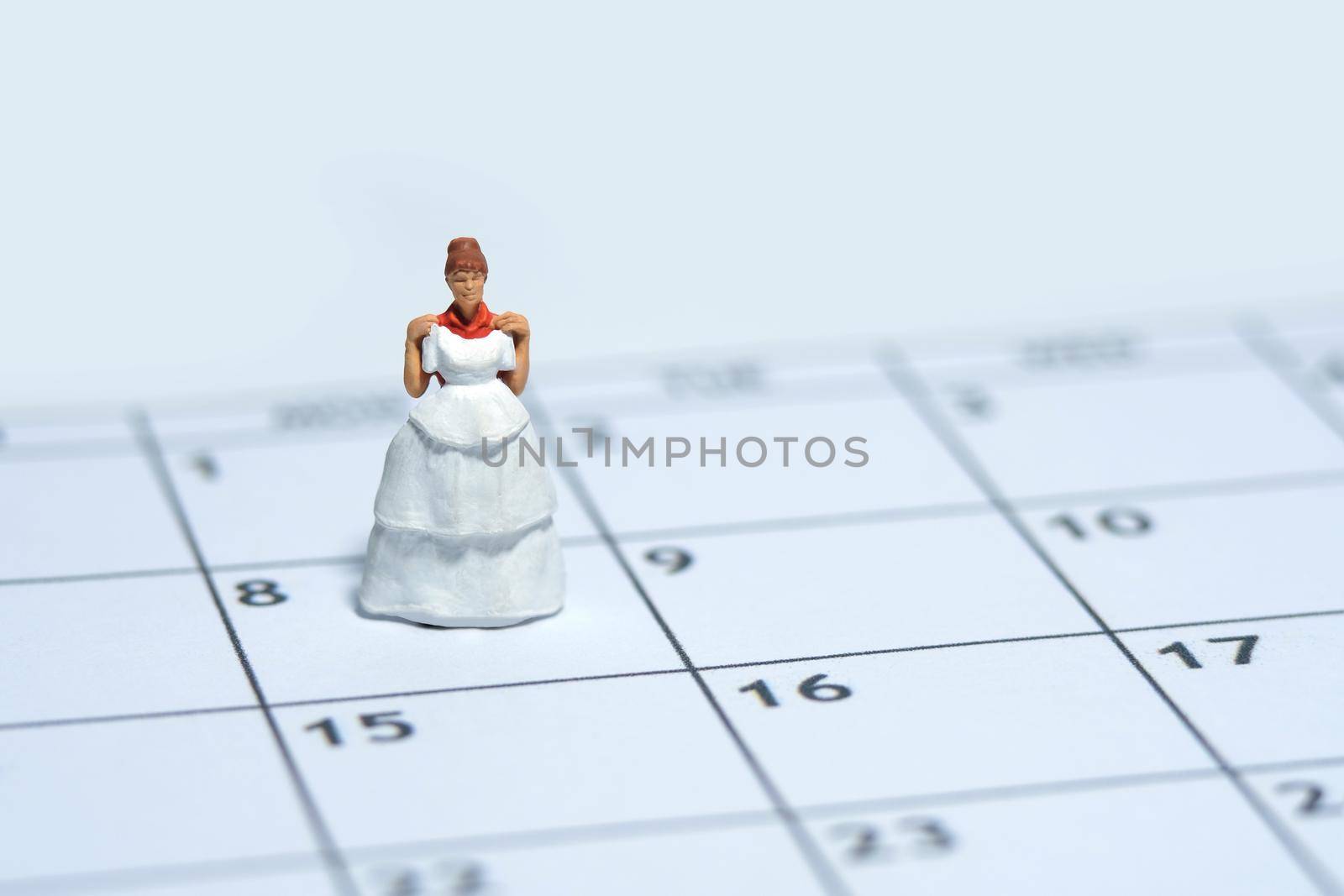 Woman miniature people stand above calendar while holding wedding dress, fitting day concept. Image photo by Macrostud