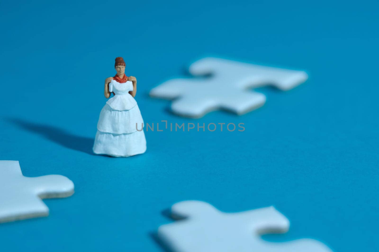 Wedding dress alternative. Miniature people women standing in the middle of puzzle jigsaw on blue background. by Macrostud