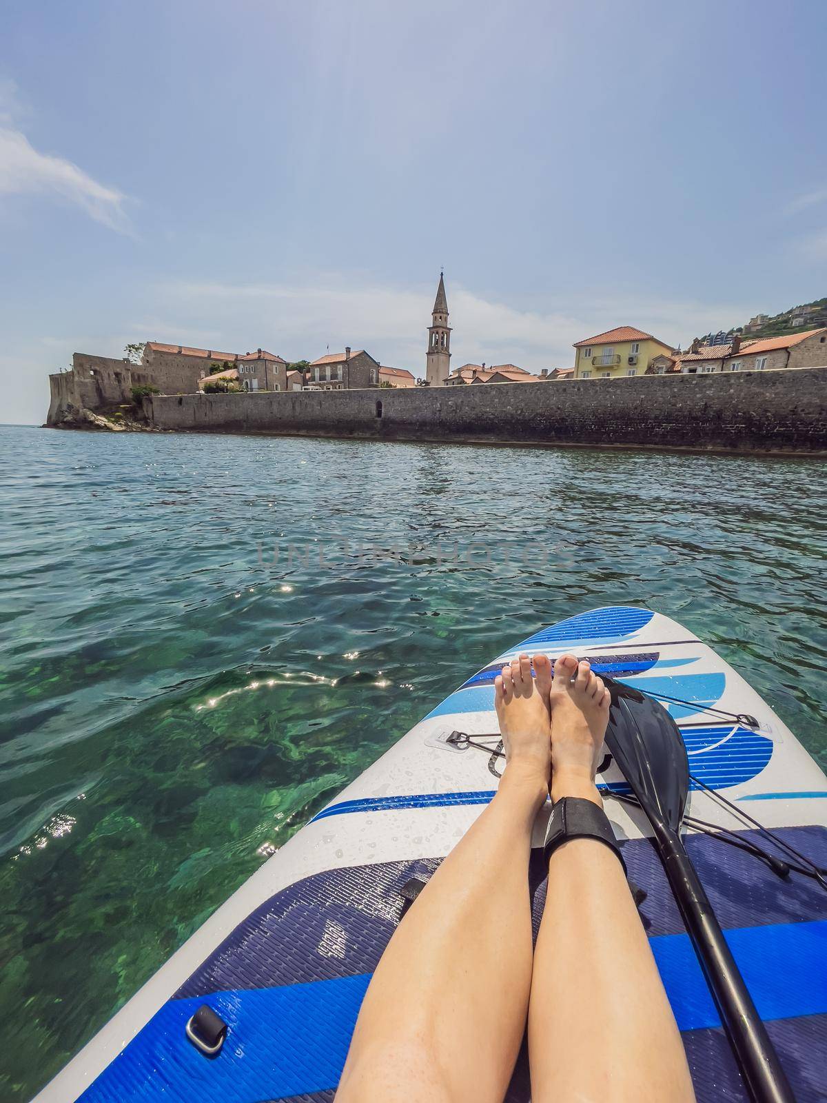 Summer holidays vacation travel. SUP Stand up paddle board. Young woman sailing on beautiful calm lagoon along Budva old town.
