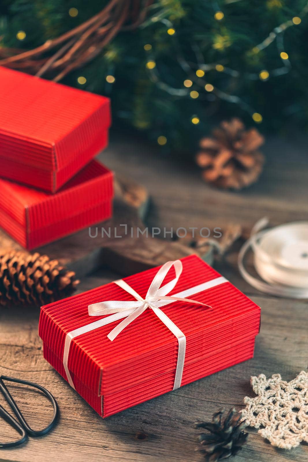 Christmas presents preparation, wrapping a red gift box with white ribbon on the wooden table