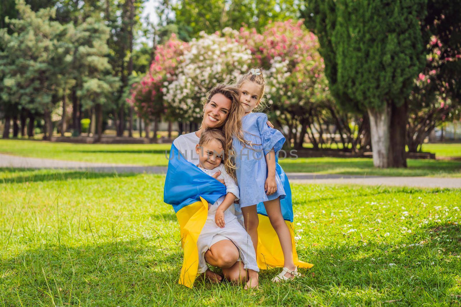 Ukrainian mother with two children with flag of Ukraine. Outside. Concept of problem of war in Europe, supporting of families and children, migrants, emigration, patriotism, motherhood, Ukrainian women.