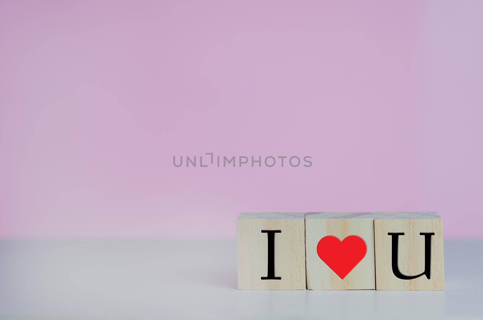 Wooden cubes with i love u symbol heart on the pink background and copy space.