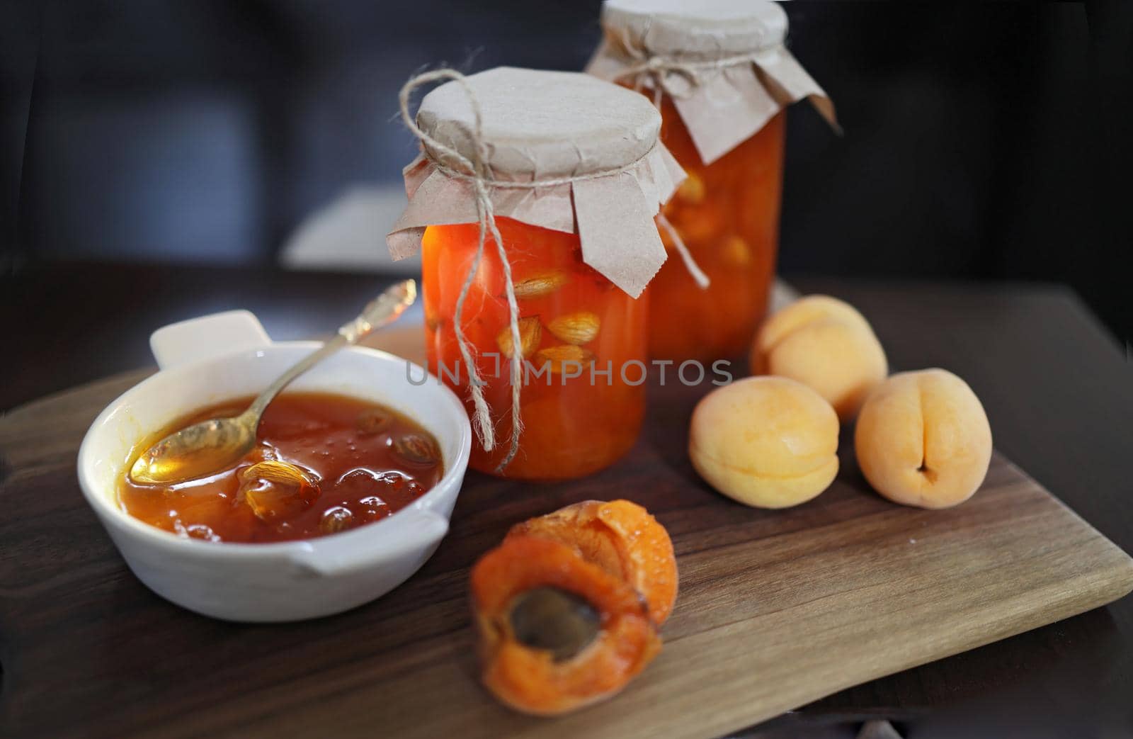 Apricot jam in glass jars on a wooden surface, a small white plate with jam and a miniature spoon. Sunshine, amber jam.