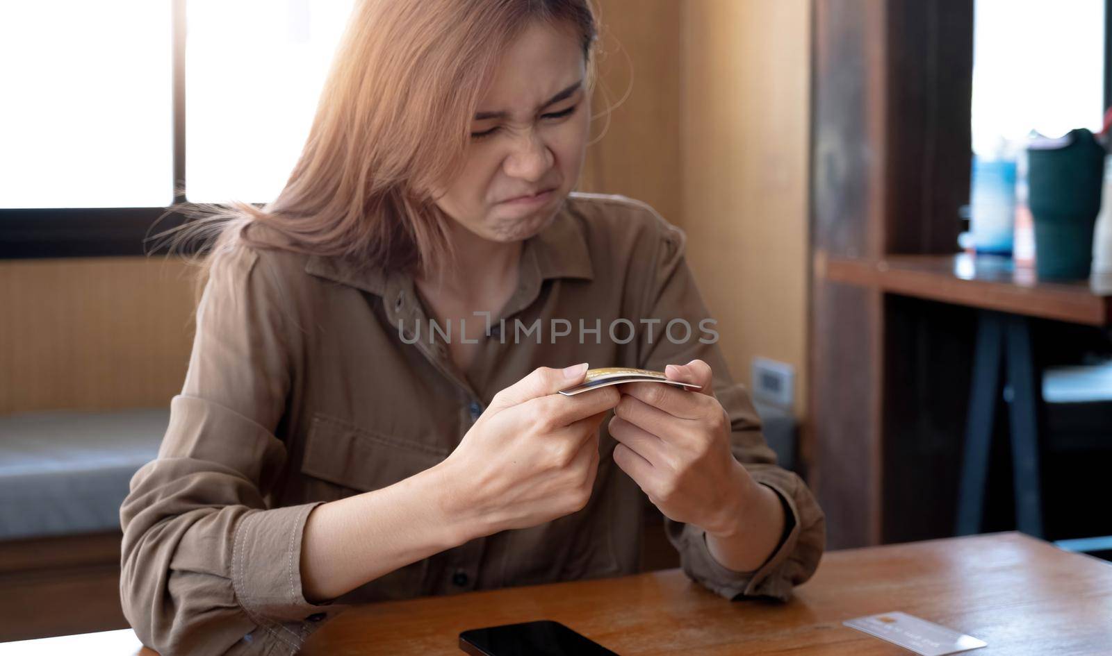 Angry and furious millennial asian woman breaking a credit card or debit card with her hands, having a financial problems. by wichayada