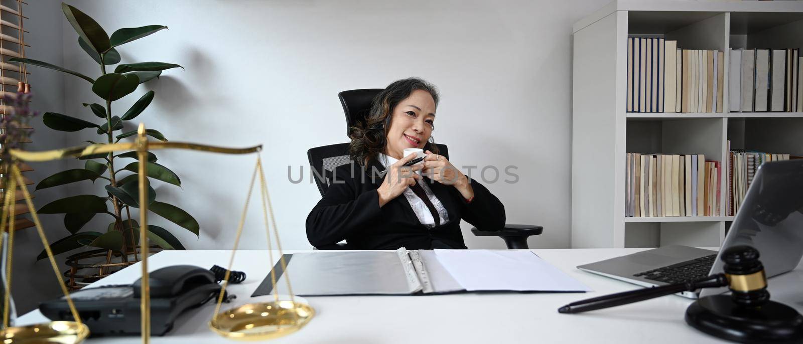 Mature female lawyer drinking coffee, resting at her personal office.