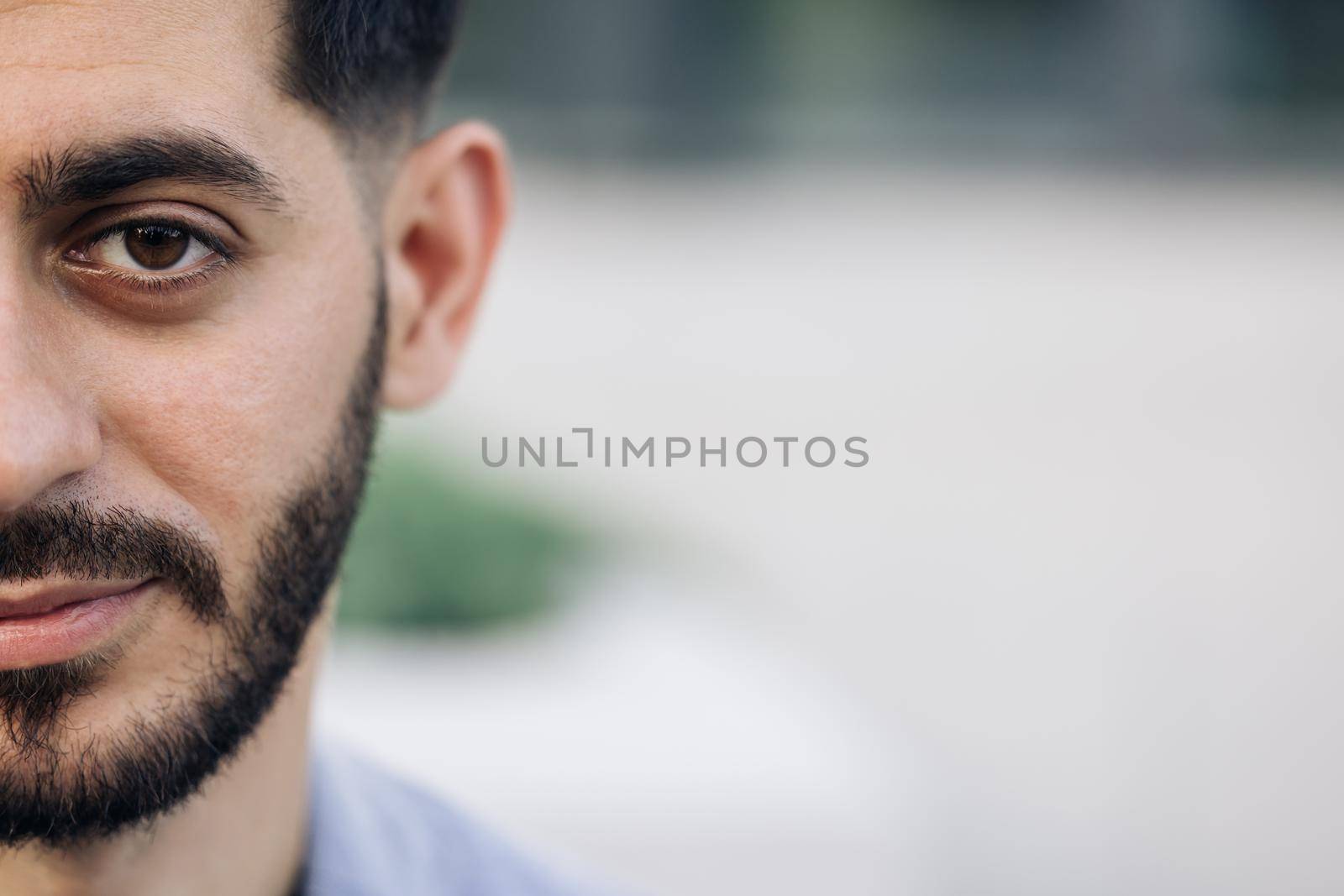 Half face portrait of young man with beard. Half face of upset bearded caucasian young man looking straight to camera while standing outdoors in empty town.