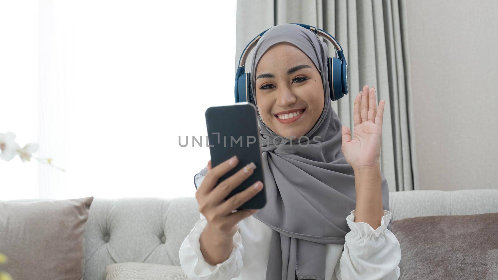 Attractive millennial Asian Muslim woman having a video call from her friends in the living room..