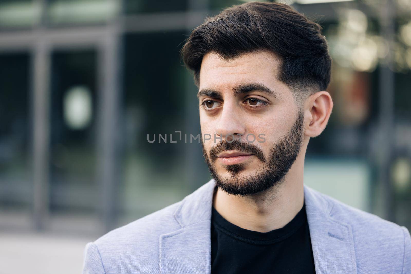 Portrait of bearded handsome young caucasian businessman standing look at camera serious outside near business center. Successful career attractive manager handsome confident.