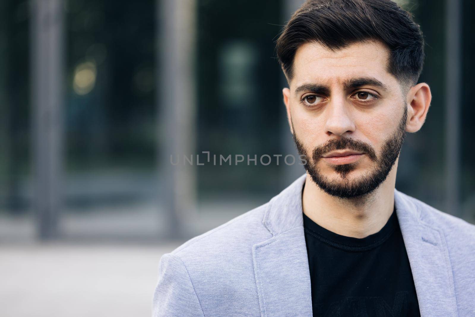 Gorgeous young bearded handsome business man in formal wear serious looks at camera outside business district. Confident guy. Attractive people. Portraits.