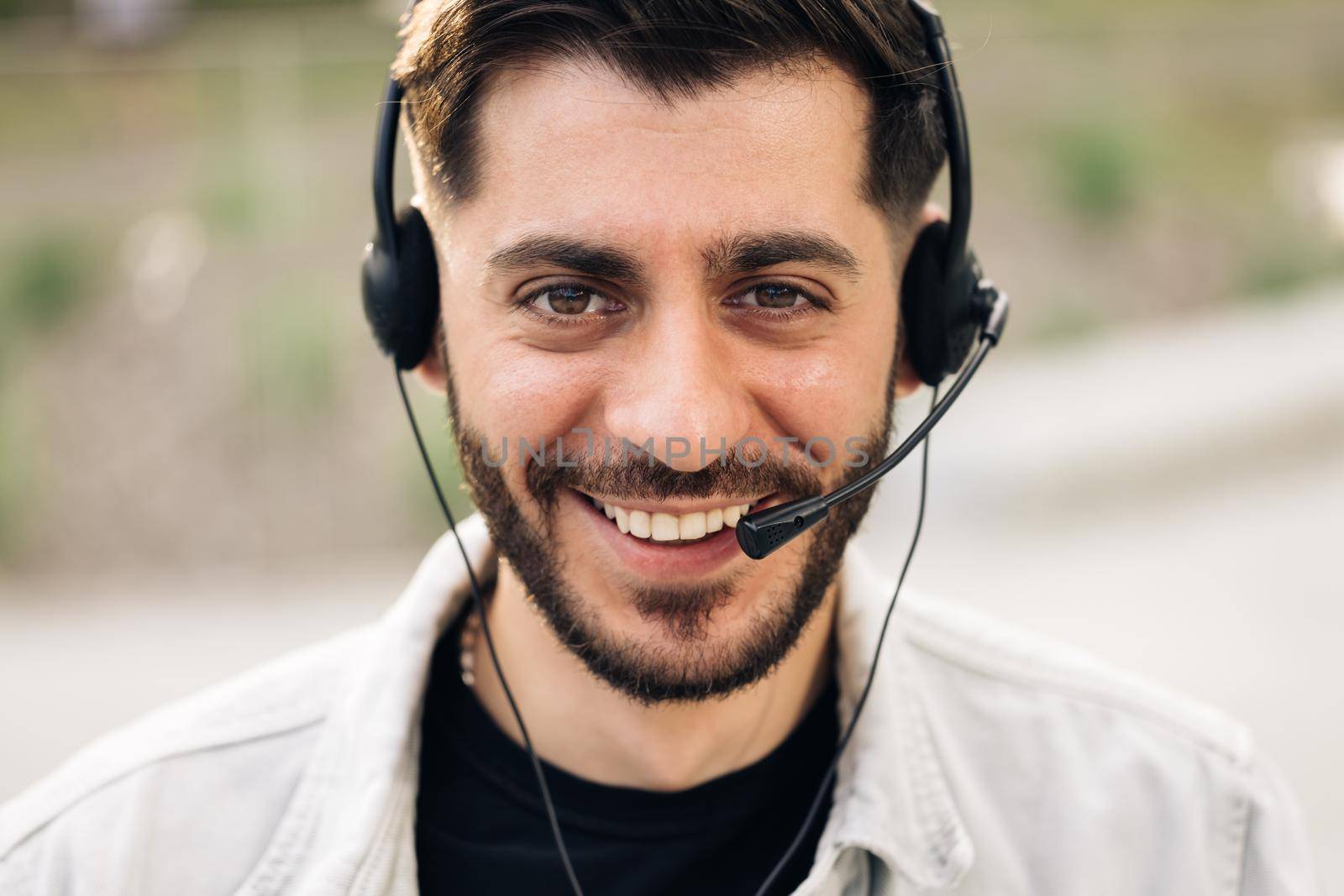 Close up of Face handsome man operator look at camera smile taking calls smile outdoor call center office business worker computer corporate headset job service group finance phone. by uflypro