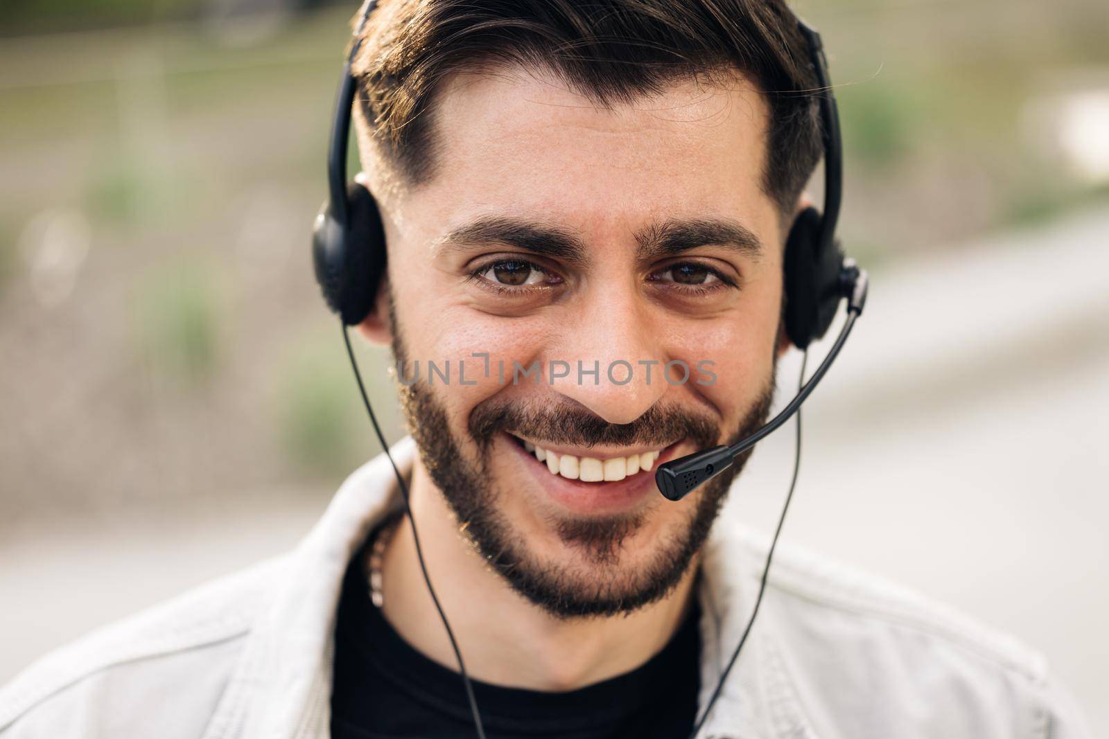 Close up of Face handsome man operator look at camera smile taking calls smile outdoor call center office business worker computer corporate headset job service group finance phone.