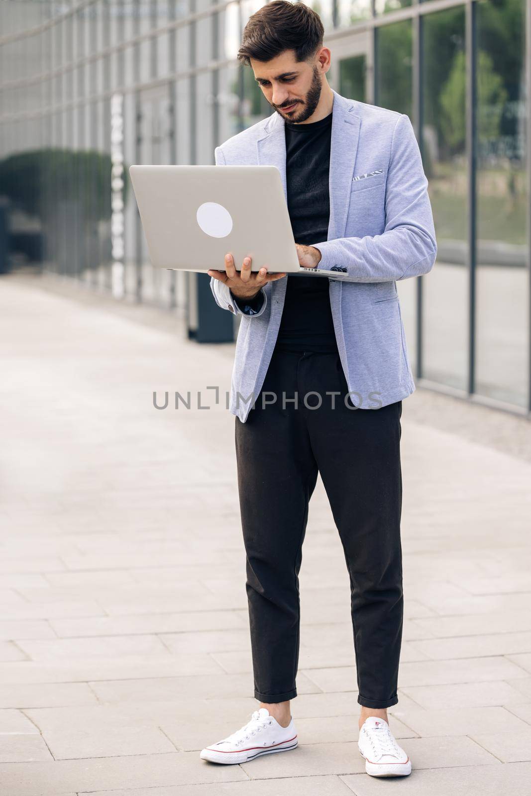 Young bearded caucasian handsome man trader working at laptop checking stock market data, looking at computer and smiling. Male successful broker with smile. Businessman.