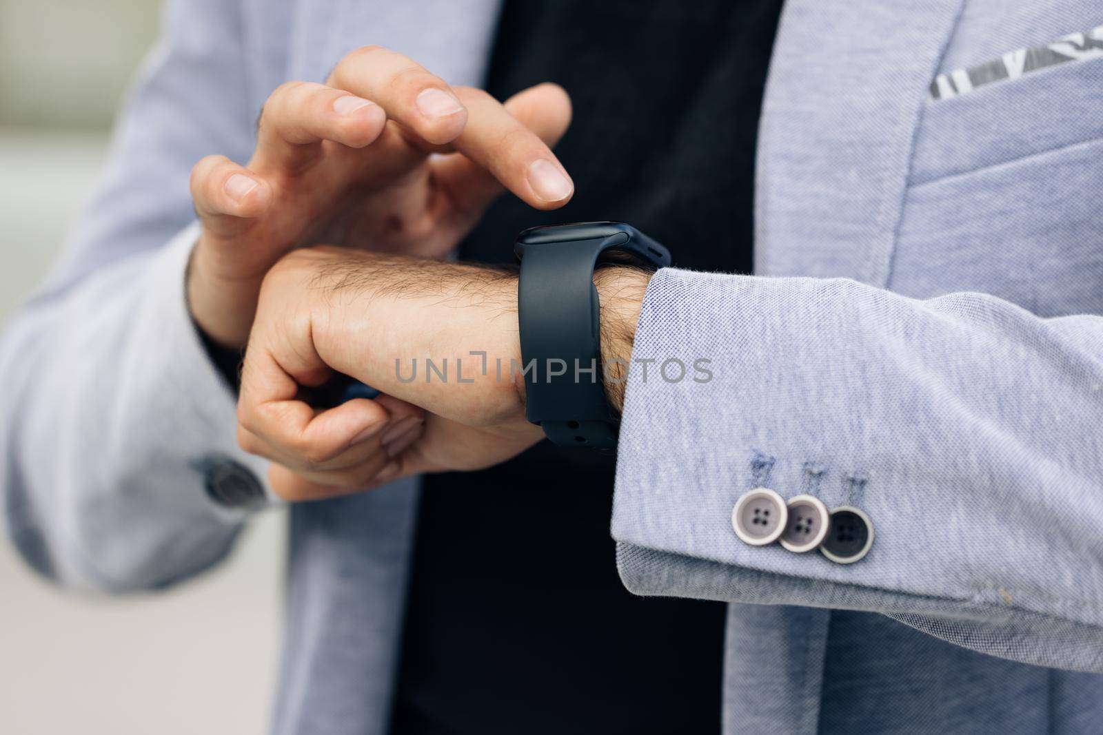 Unrecognizable male hands using smart watch. Businessman uses a smartwatch on his hand and keeps track of the time on the display. Close up of businessman checks smartwatch. Jacket formal wear. by uflypro