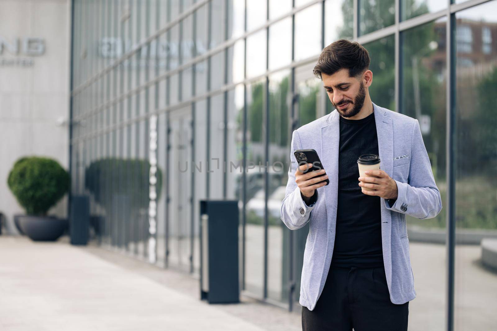 Gorgeous bearded businessman using mobile phone for texting during way to office in financial district, successful male proud ceo smiling during cellular messaging