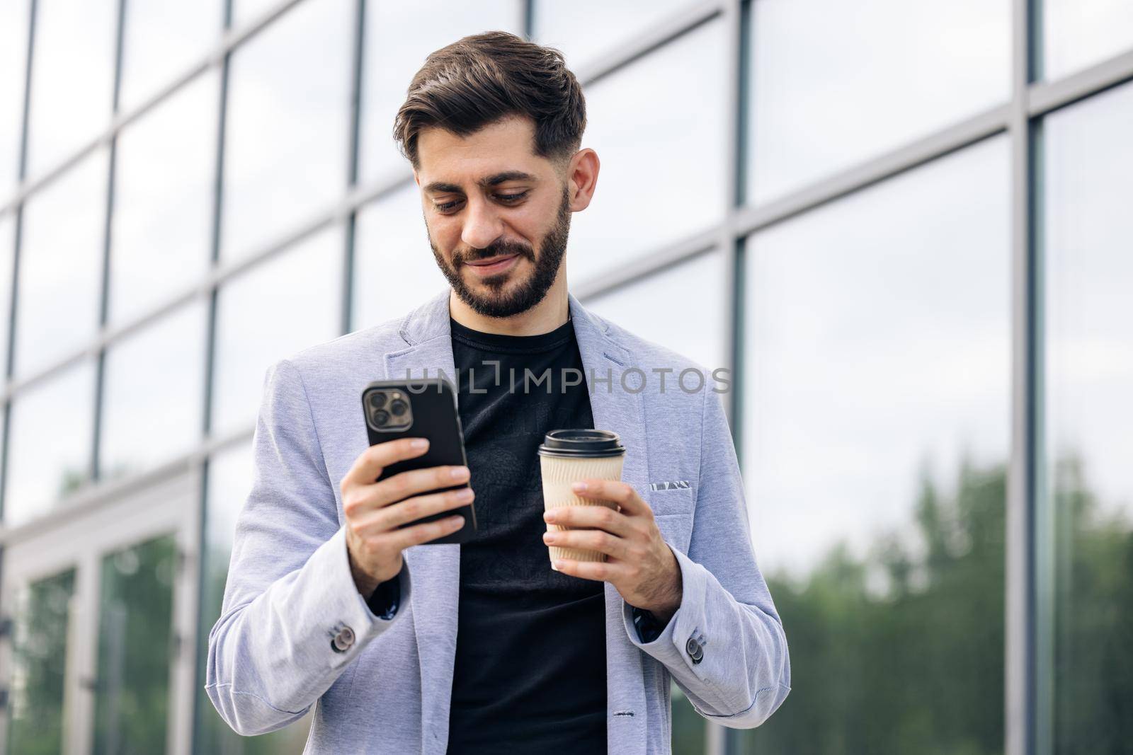 Gorgeous bearded businessman using mobile phone for texting during way to office in financial district, successful male proud ceo smiling during cellular messaging. by uflypro