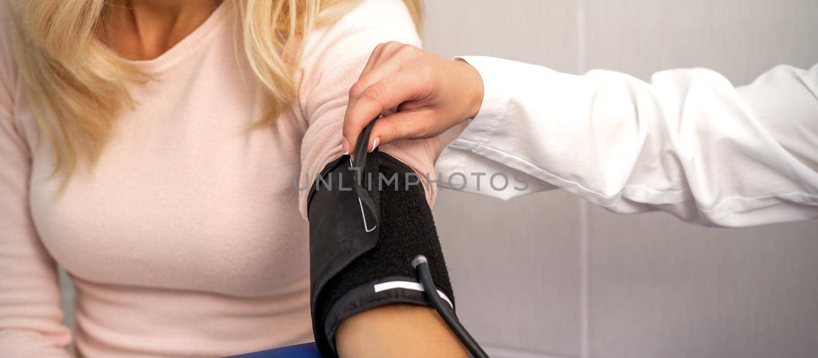 Nurse or female doctor puts on tonometer on arm of young woman in the hospital