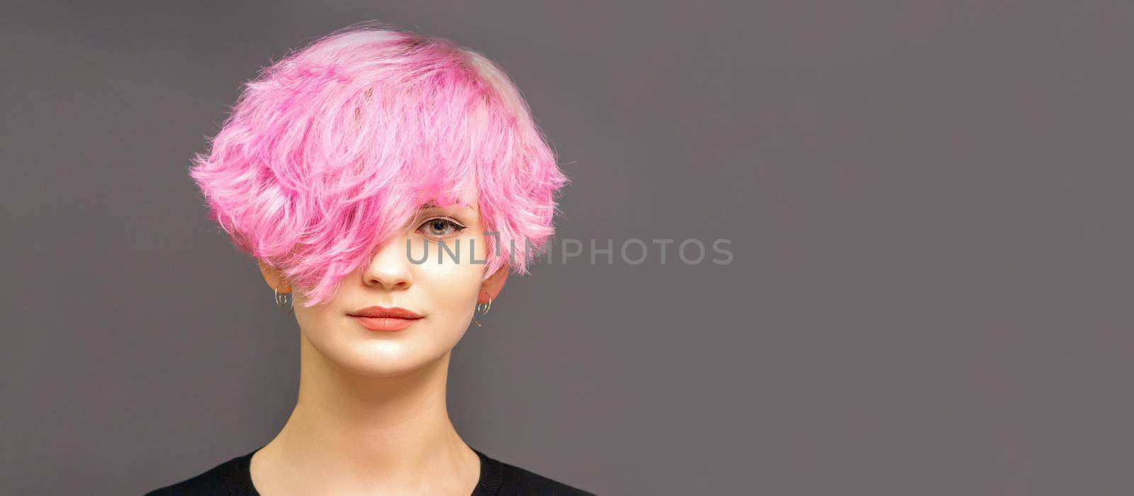Portrait of fashion model young woman with stylish dyed pink hair in black clothes on dark background
