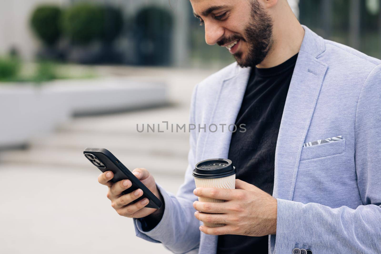 Young elegant bearded man using social media application on smartphone text messages receive news smiling outdoor. People portraits. Technology by uflypro