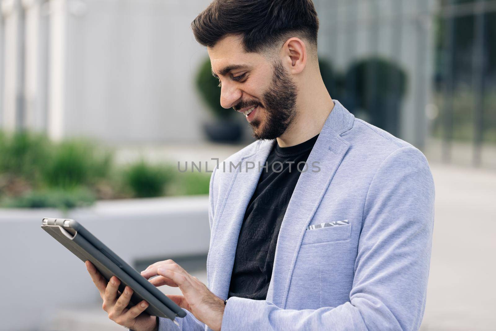 Happy face looking tablet screen outdoors. Elegant male chatting online with digital device outside. Businessman holding tablet in hands using business apps on tablet computer by uflypro