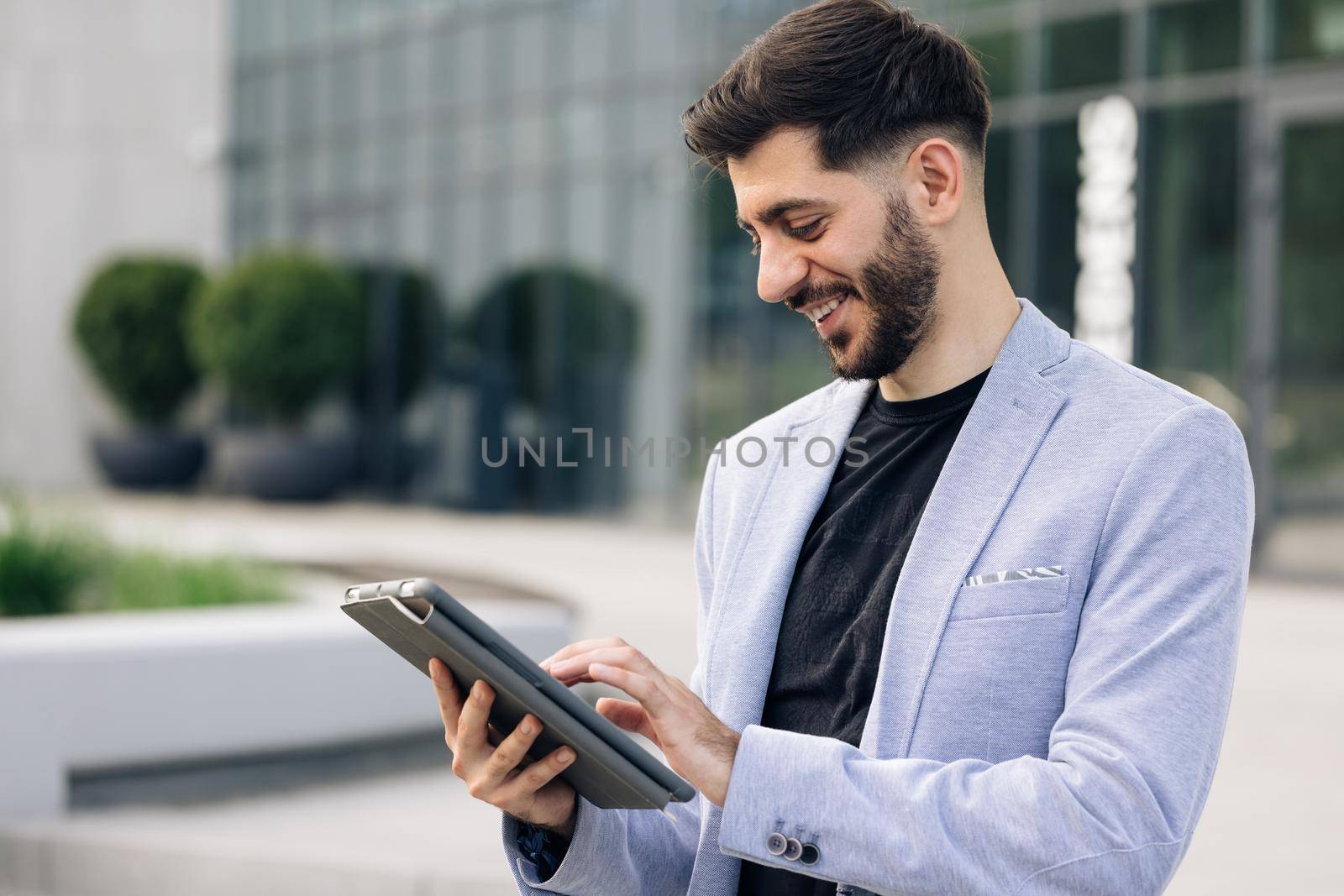 Beautiful young man engaged in business using tablet computer reading financial news online. European hairstyle. Corporate people by uflypro