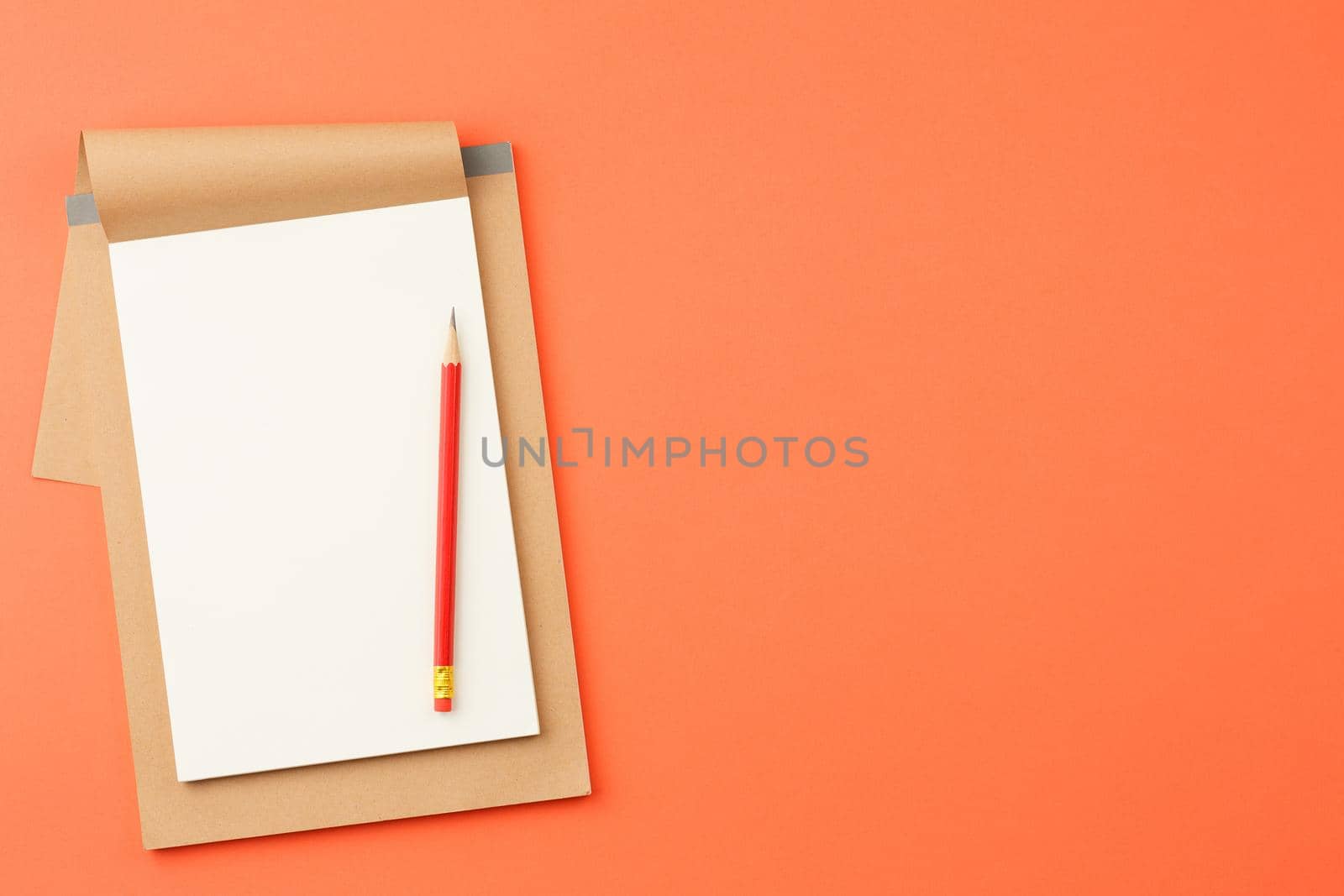 Craft notebook with white sheets, red pencil on orange isolated background top view.