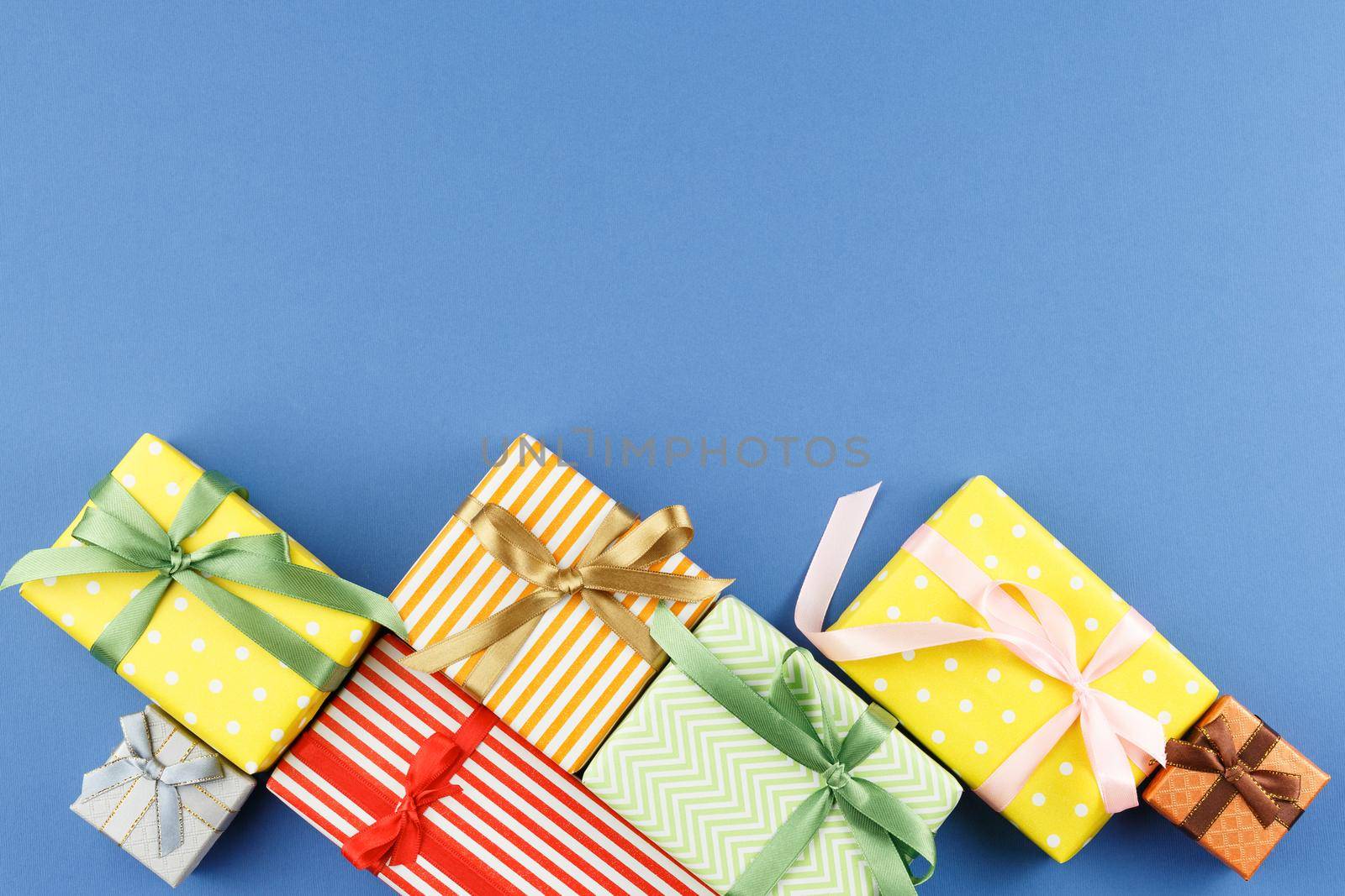 Gifts in colorful wrapping paper with ribbon bows on blue isolated background. Flat lay. Festive present concept. Top view.