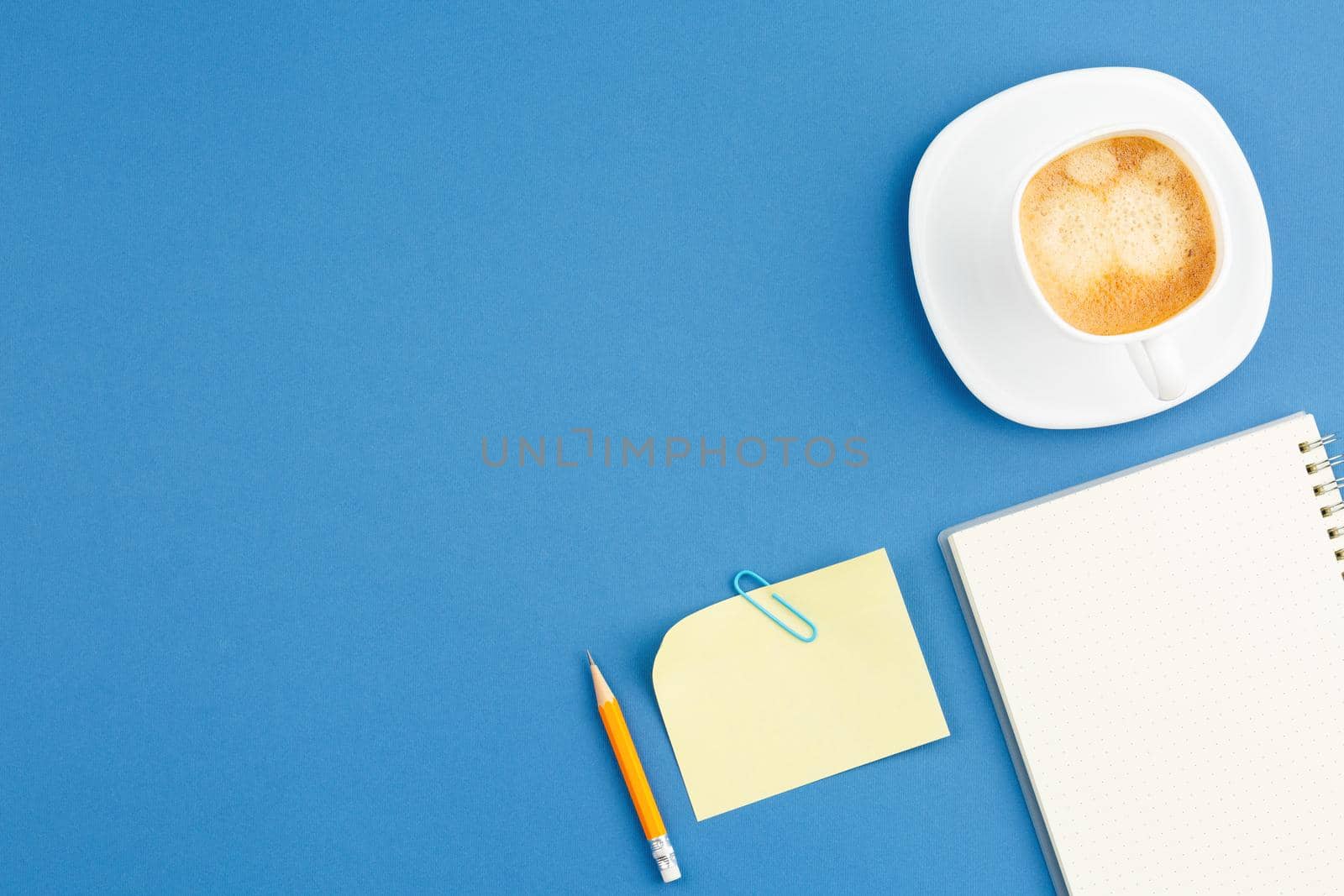 Open spiral notebook with pencile and cup of coffee on blue background. Flat lay, top view.