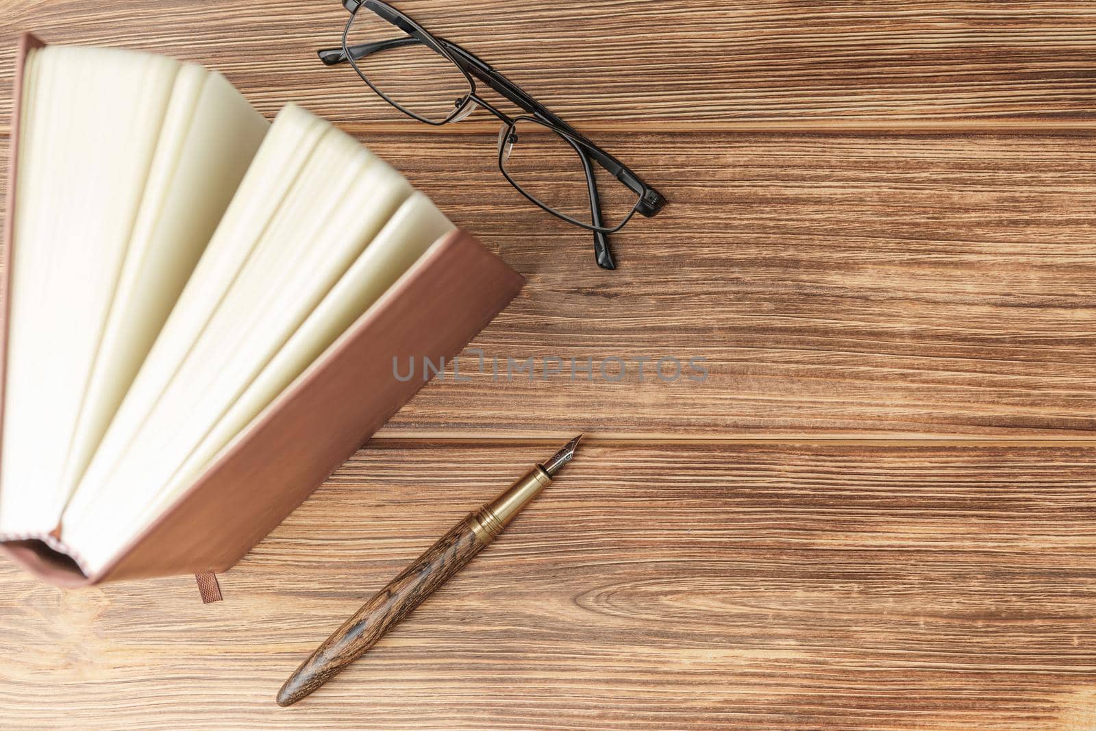 Upright book notebook notepad glasses and wooden gold fountain pen on light wooden background top view close up.