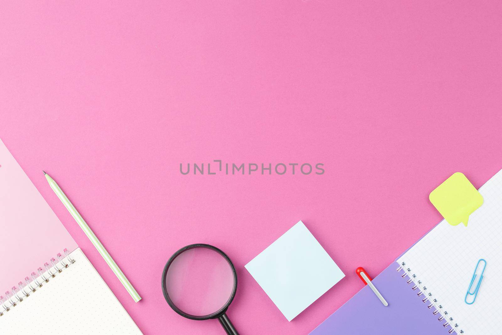 Open school notebook with magnifying glass and pencil on pink isolated background. Top view. School desk concept. Flat lay.