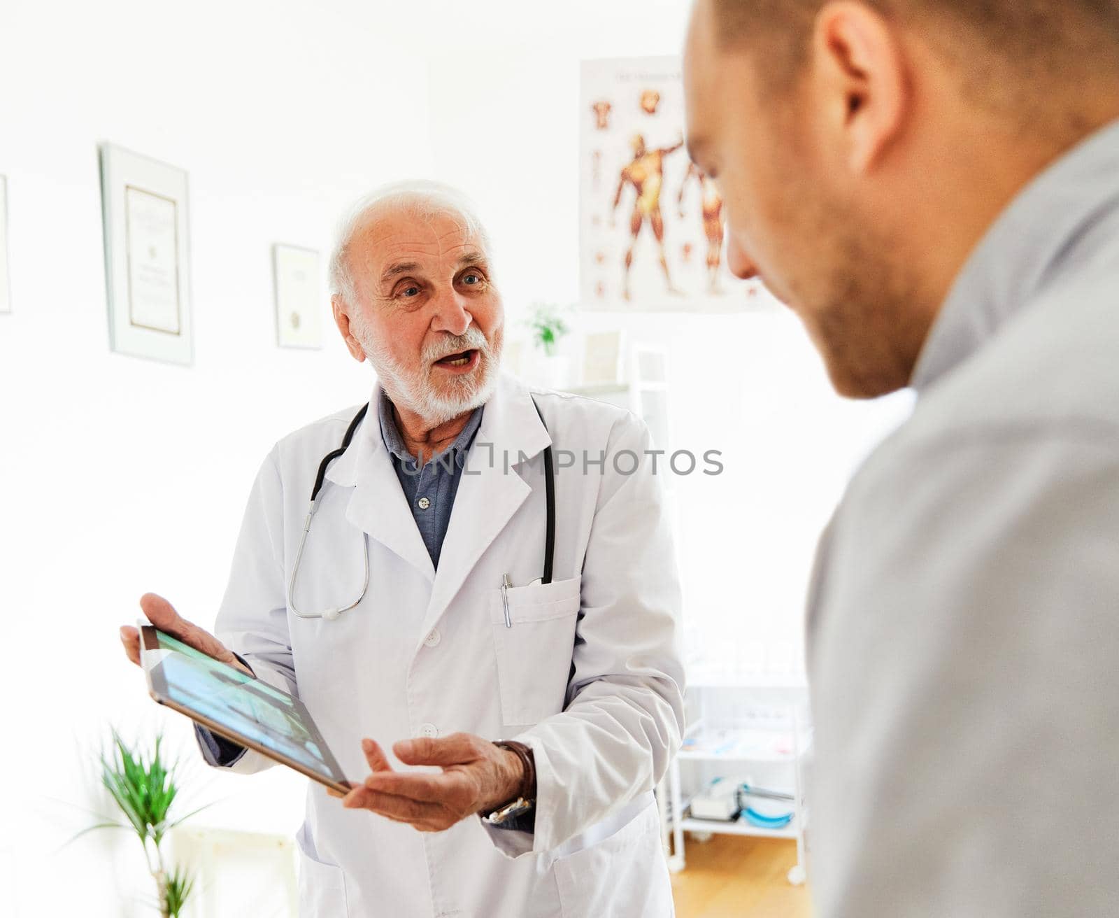 Senior doctor holding tablet talking to young man in his office in clinic