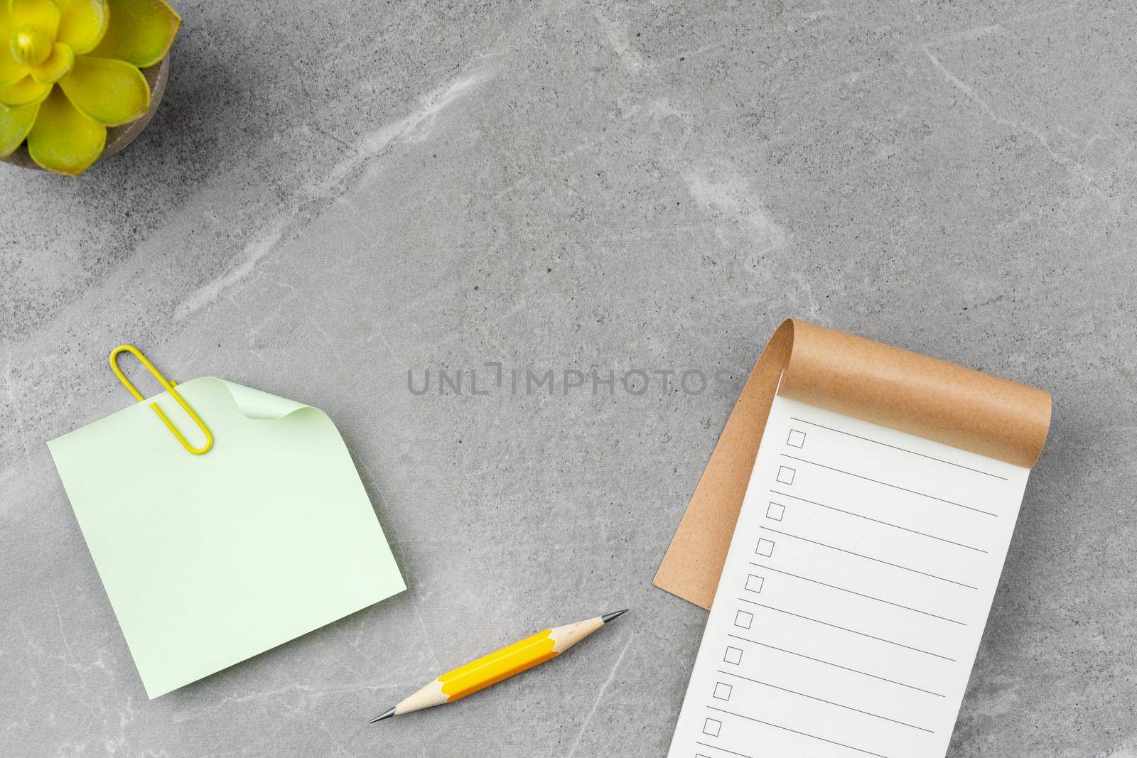 Open notepad, pencil, notepaper and potted plant on gray marble background. Top view. Office desk concept.