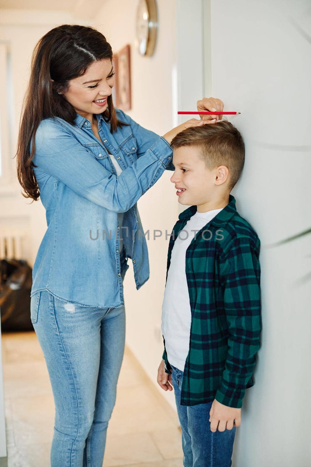 Mother measuring the height of her son on the wall at home