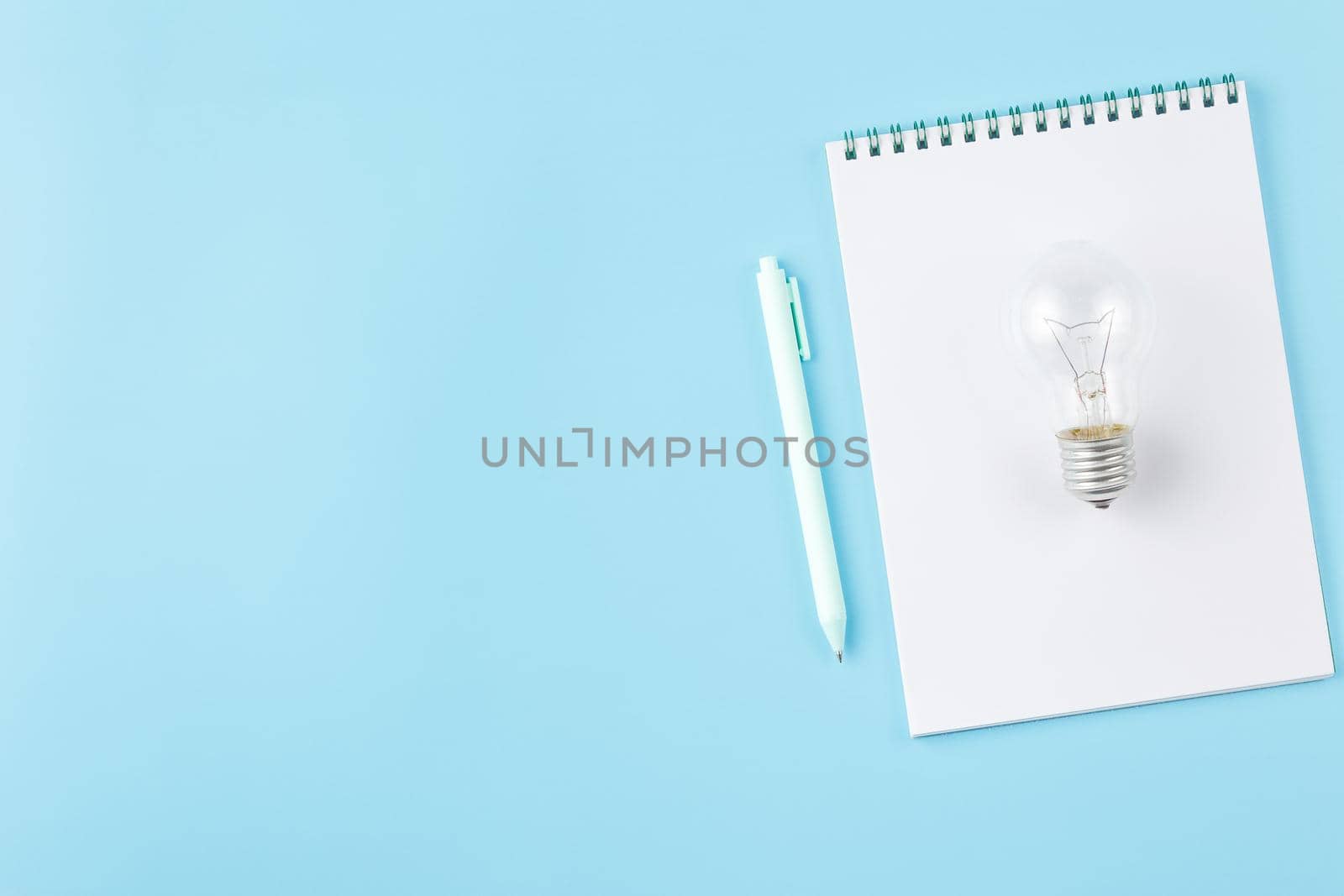 Light bulb with a spiral notepad and pen on a blue background. Initiative of ideas concept of a business or some activity.