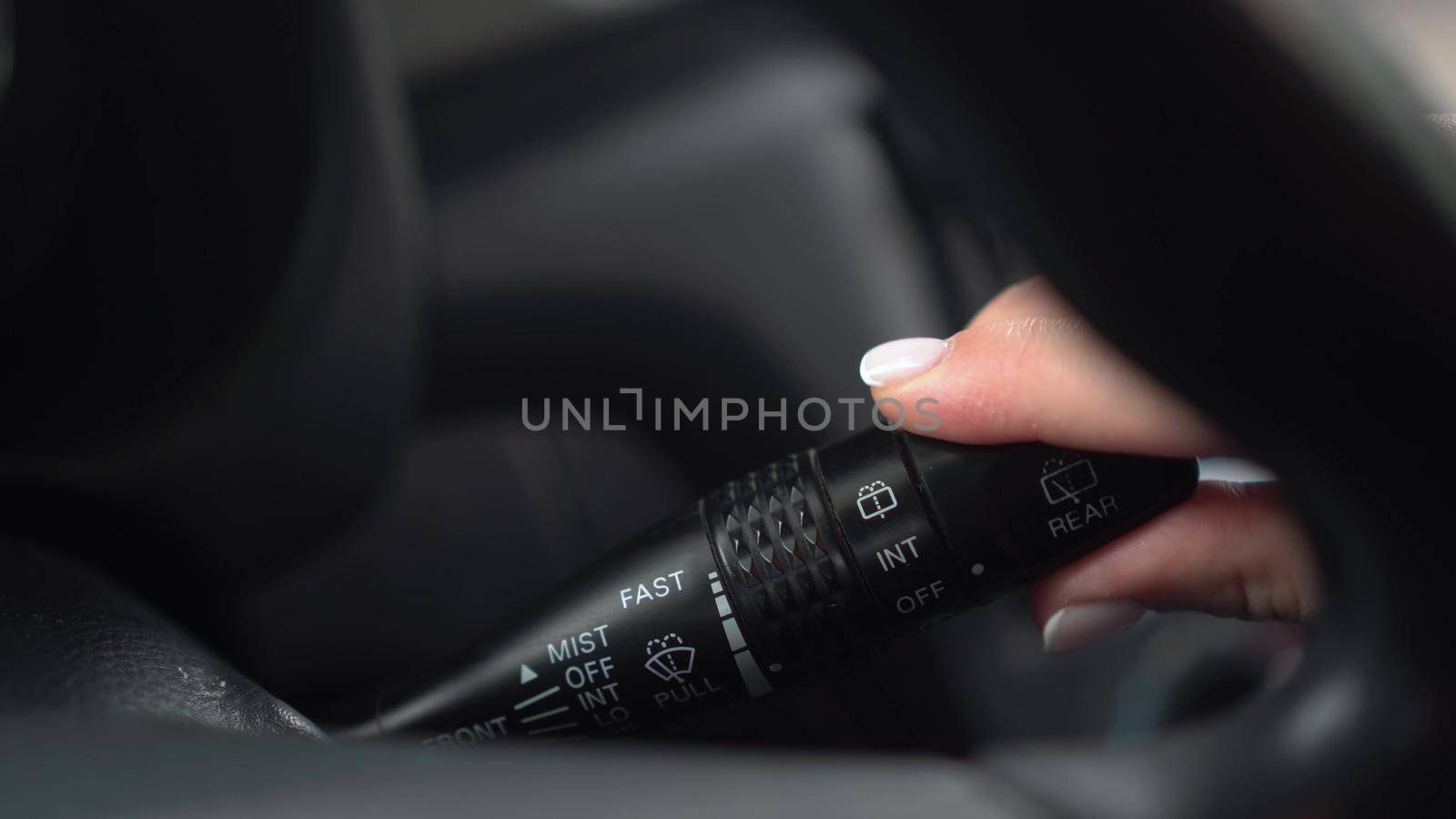 A woman turns on the wipers by turning the lever in the car. Automotive panel close-up. 4k