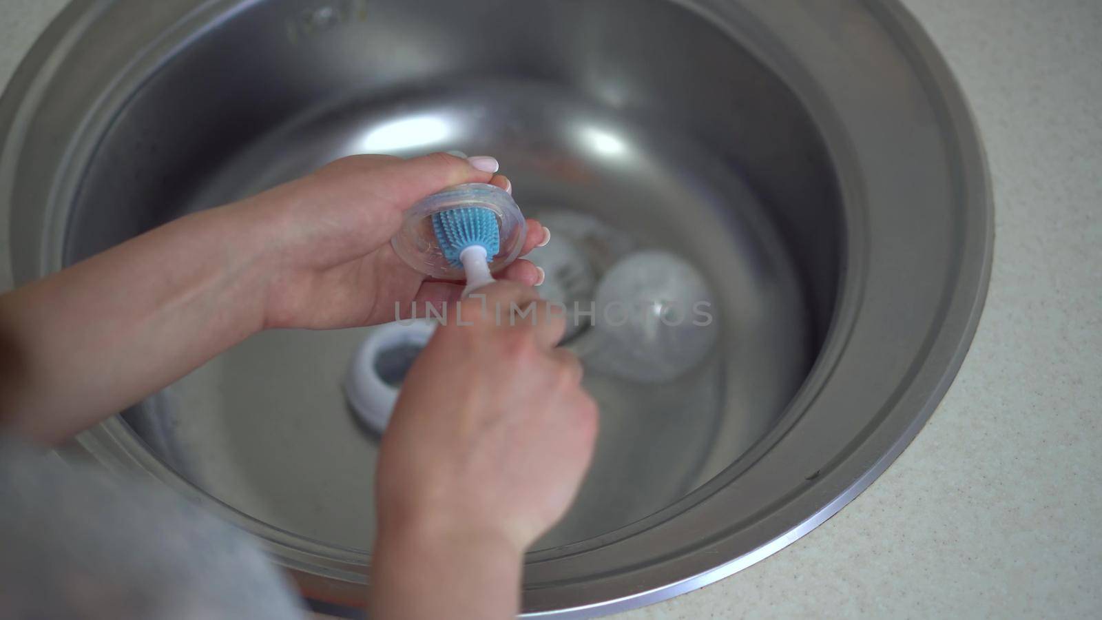 A young mother cleans the nipple from a baby food bottle with a special brush. Close-up hands. 4k