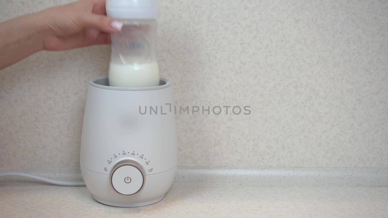 A woman puts a bottle of food into a bottle warmer. Apparatus for rapid heating and stirring of infant formula. 4k