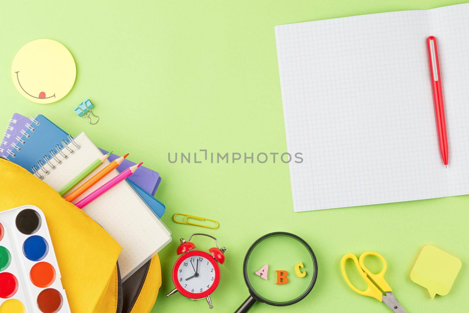 School backpack with spiral notebooks and a pen on a green background. Back to school concept. Top view. Open notebook, alarm clock and note paper on the desk. Flat lay.