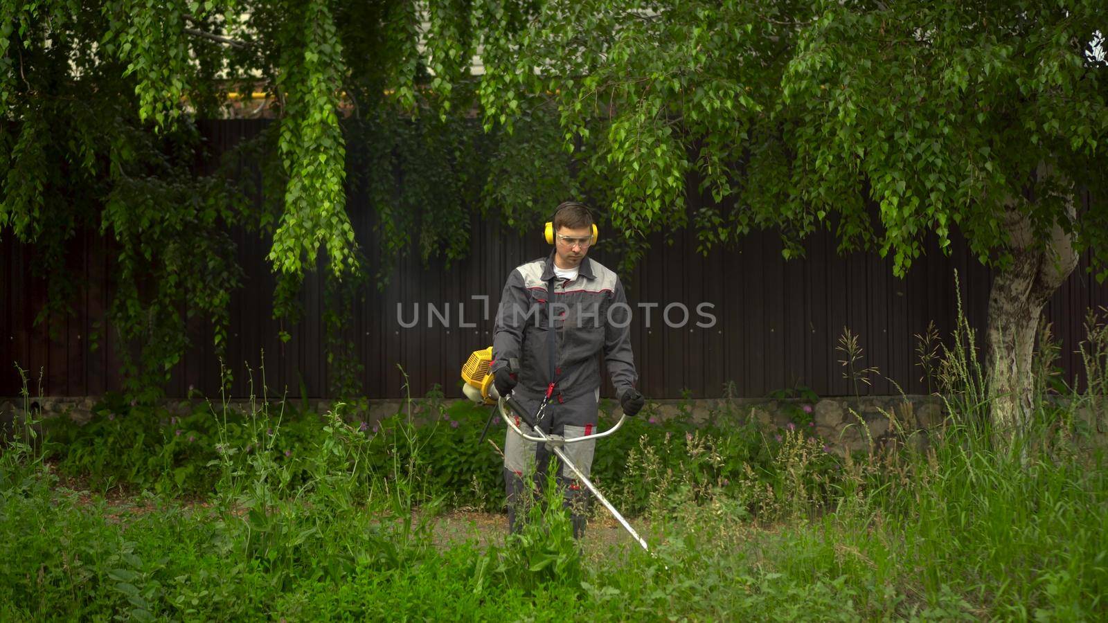 A young man from the special services mows the lawn with a petrol trimmer. A man in glasses and headphones with a lawn mower in his hands. 4k