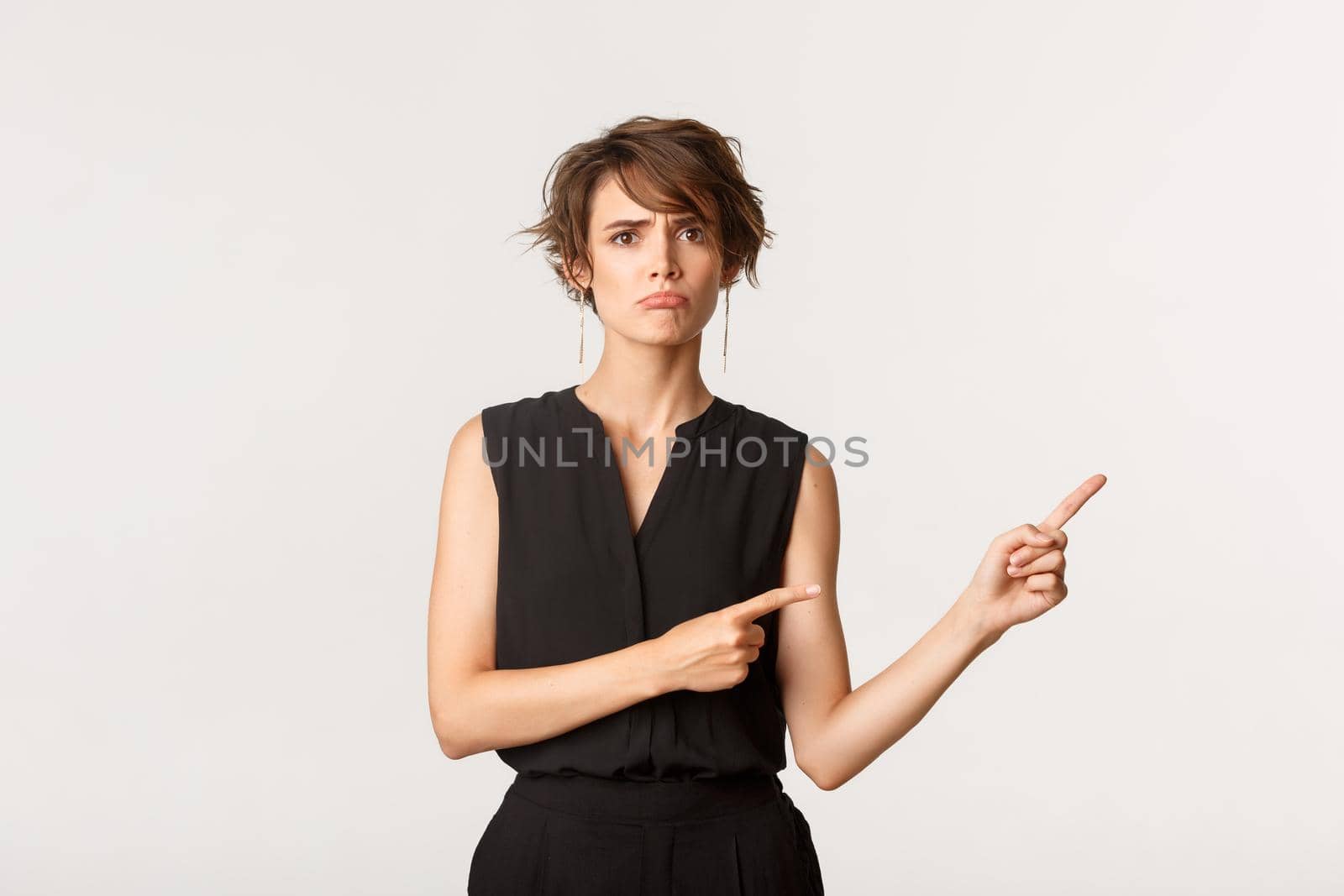 Sad young woman complaining, pointing fingers right at banner and sulking upset, white background.