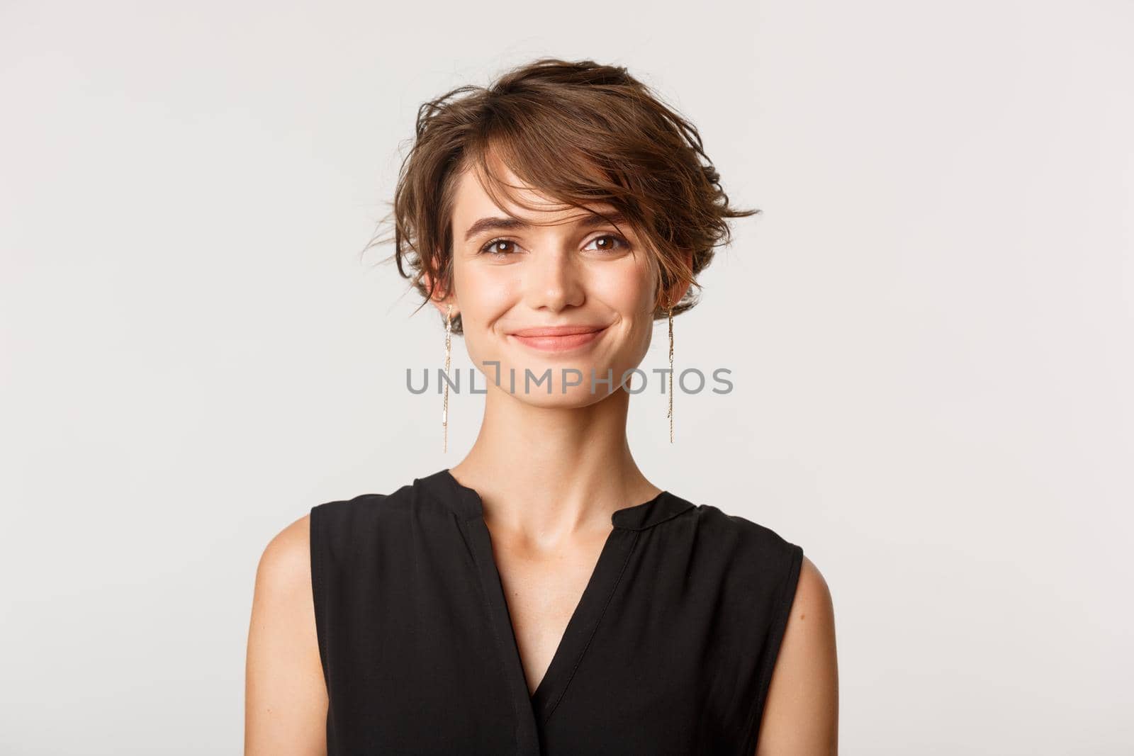 Close-up of attractive fashionable woman smiling at camera, standing over white background.