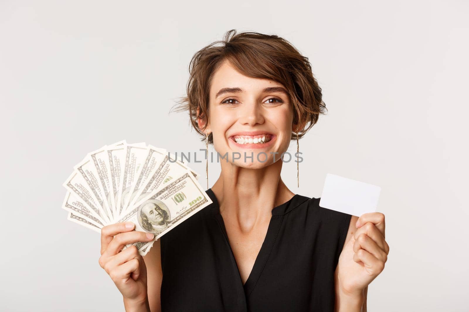 Close-up of successful businesswoman smiling, showing credit card and money, standing over white background.