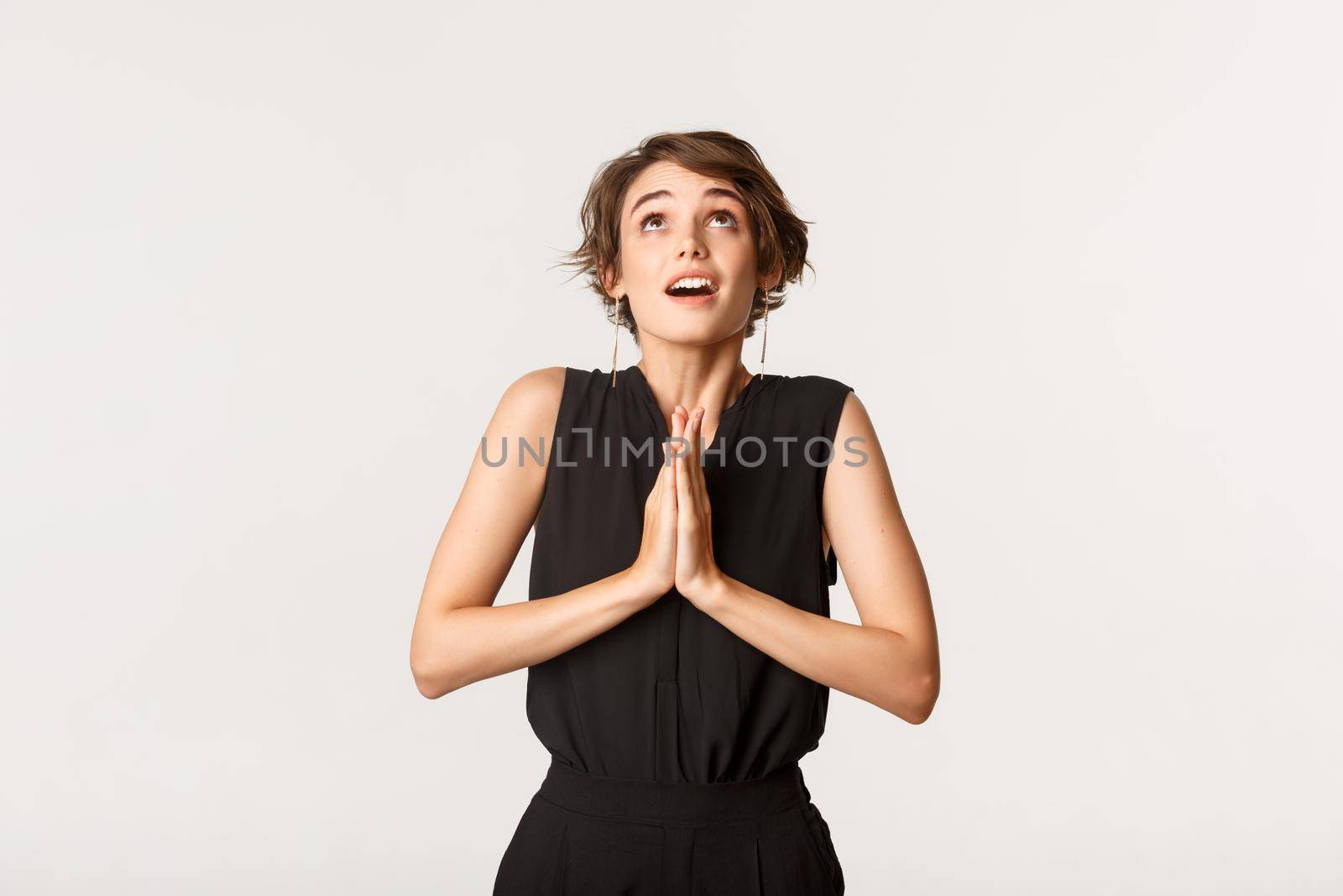 Image of hopeful praying girl clasp hands together and looking up, pleading to God, standing white background.