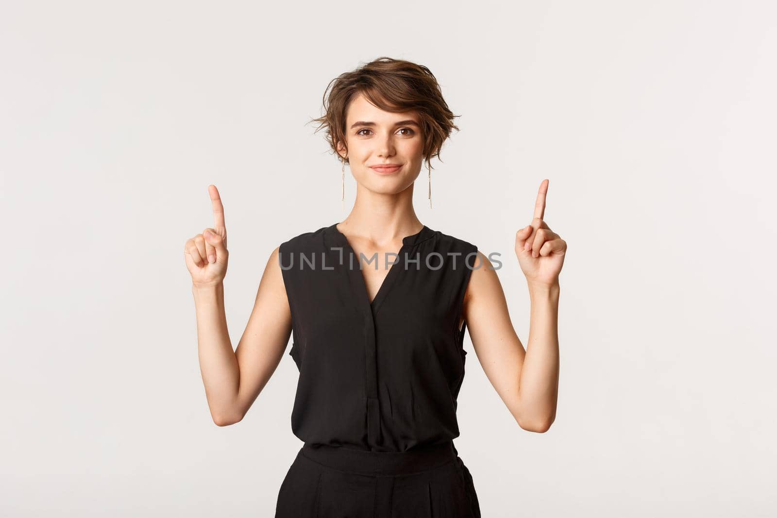 Image of confident attractive and stylish young woman pointing fingers up, showing logo, white background by Benzoix